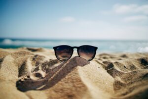 Een zonnebril ligt op een hoopje zand op het strand... wat voor verhaal verzin jij bij deze foto? Doe mee aan de schrijfwedstrijd juli 2022 van schrijfcoach Kelly Meulenberg. Foto door Ethan Robertson via Unsplash
